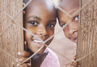 Two children peeking through a fence