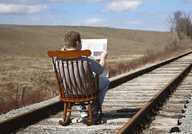 A foolish man reading a newspaper on railroad tracks