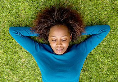 The woman is lying supine in the grass.