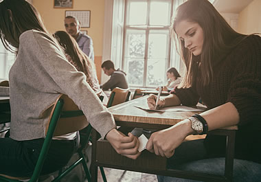 The students are passing a note in an inconspicuous way.