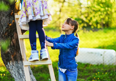 The girl is stabilizing the ladder for her friend.