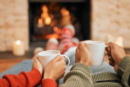 couple drinking mugs of hot chocolate in front of a fireplace