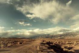 ufo spaceship hovering over a desert road with puffy clouds