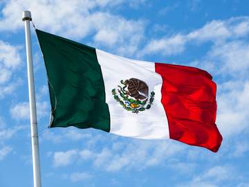 flag of mexico waving in the wind over partly cloudy sky