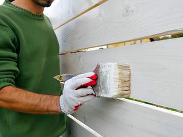 man painting a fence white with a paintbrush