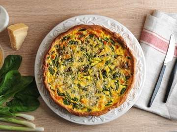 quiche made with spinach and green onions on a white plate