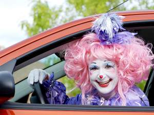 clown driving a car looks out the car window and smiles