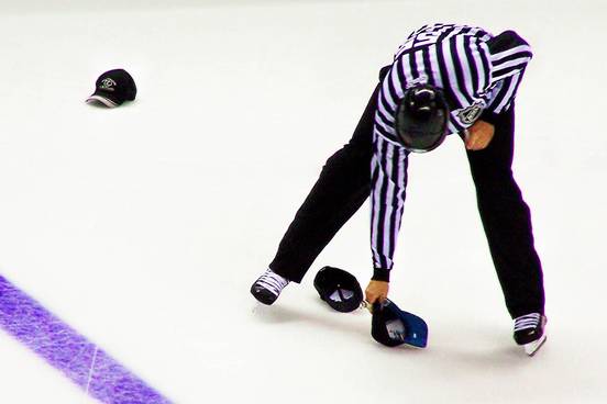 hockey official bends over to pick up hat