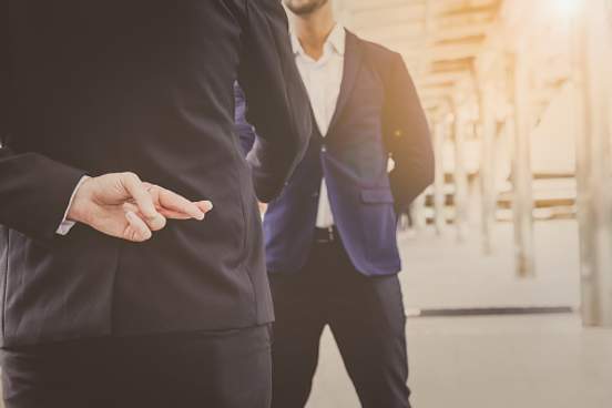 man crossing fingers behind back while shaking hands