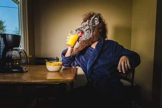 man in werewolf mask drinking orange juice