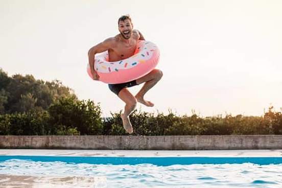 man jumping into pool with donut inflatable tube